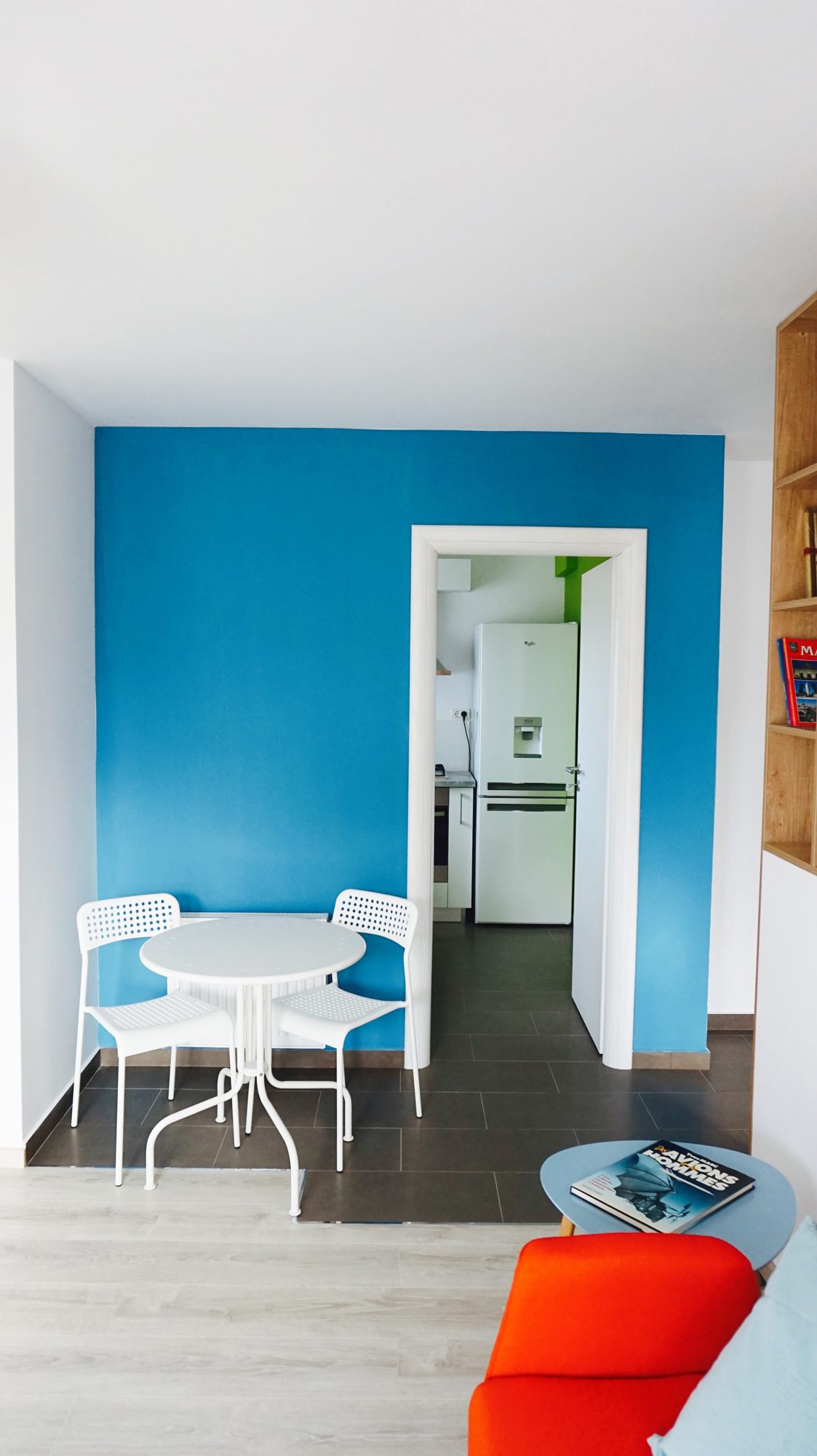 Zona de luat masa în fața peretelui albastru, cu bucătăria în spate